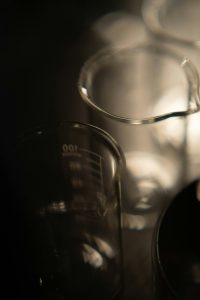 Plusieurs béchers en verre sur fond sombre — alcool et formulation en parfumerie — Noble Essence